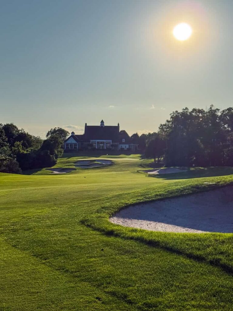 Sunset view at clubhouse behind 18th green from fairway with shadowed bunker and trees along the side