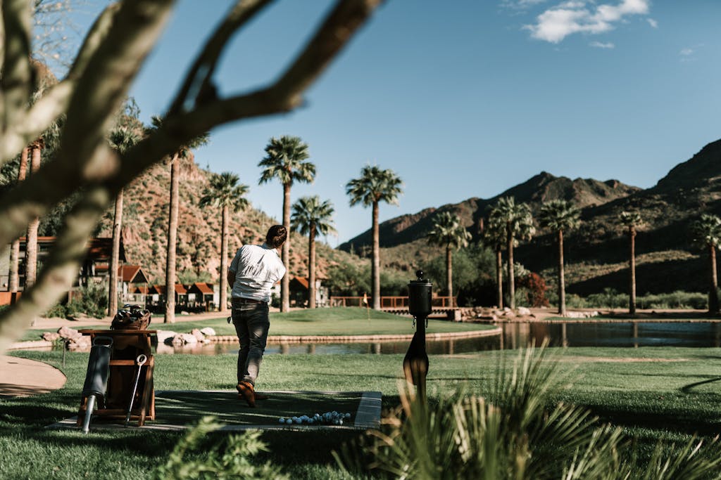 Golfer practicing swing with scenic mountain and palm tree backdrop, outdoors.